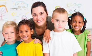 four kids lineup for photo with adult smiling behind them