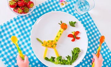 a giraffe and butterfly standing in the grass constructed out of food on a childs plate